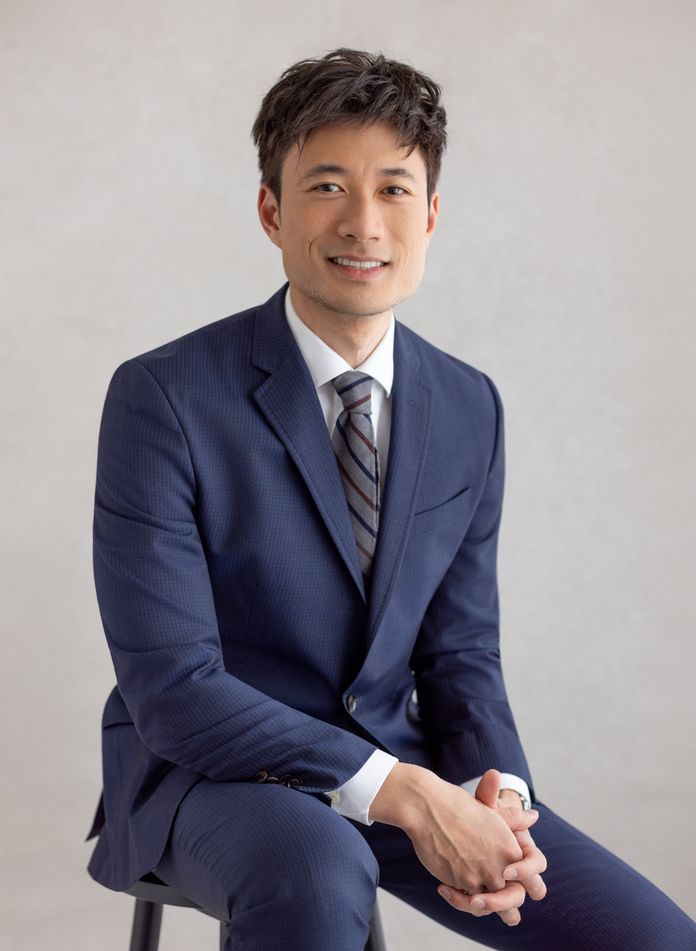 Dr. Dang wearing blue suit with a striped tie sitting on stool